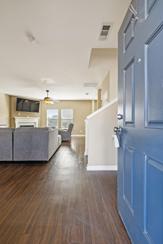 foyer entrance with baseboards, visible vents, ceiling fan, dark wood-style flooring, and a fireplace