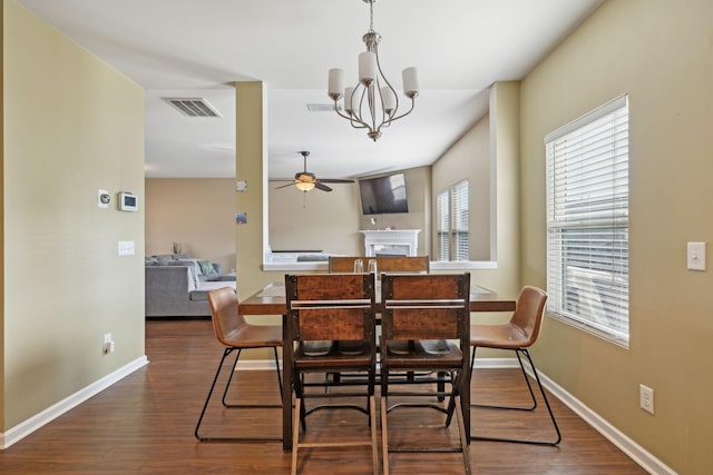 dining room with ceiling fan with notable chandelier, a fireplace, dark wood finished floors, and visible vents