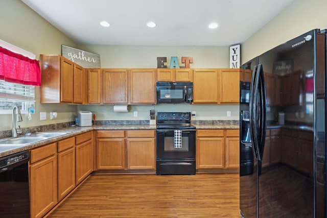 kitchen featuring black appliances, wood finished floors, a sink, and recessed lighting