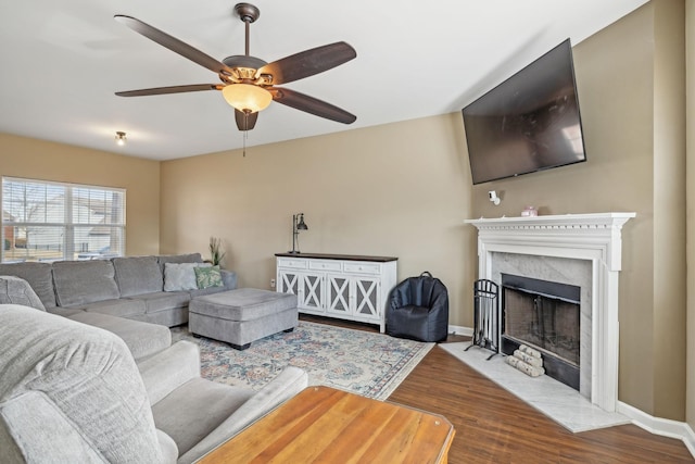 living area with ceiling fan, a premium fireplace, wood finished floors, and baseboards