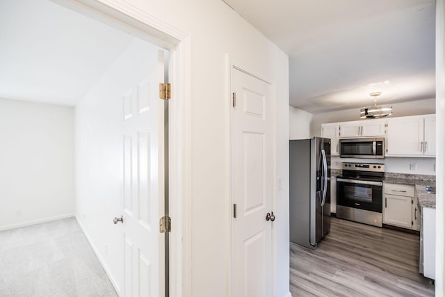 kitchen with light wood finished floors, baseboards, white cabinets, light stone countertops, and stainless steel appliances