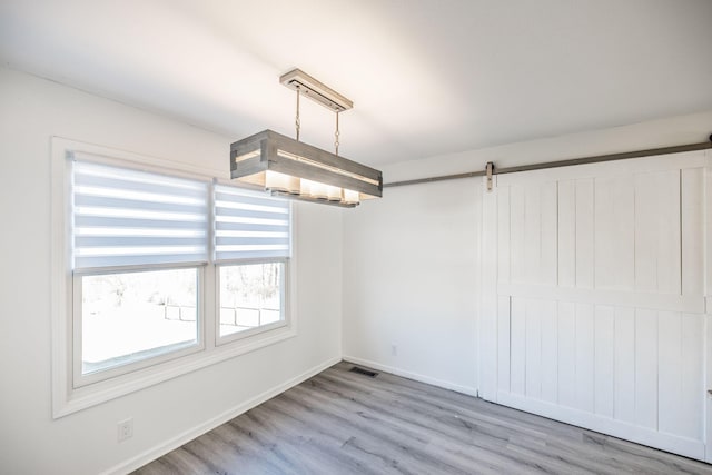 unfurnished dining area featuring light wood-style floors, a barn door, visible vents, and baseboards