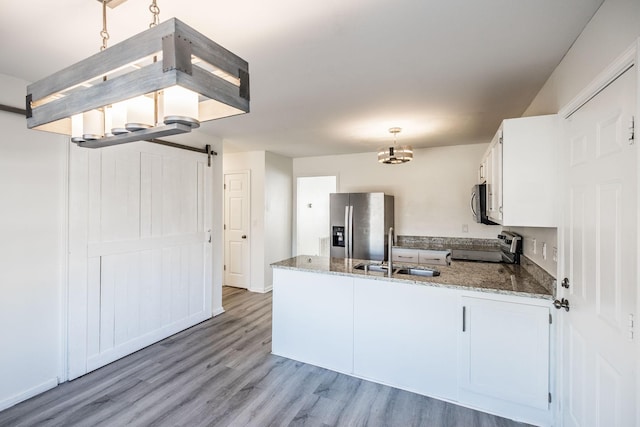 kitchen with a barn door, a sink, white cabinets, appliances with stainless steel finishes, and pendant lighting