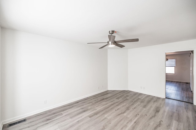 spare room with light wood finished floors, a ceiling fan, visible vents, and baseboards