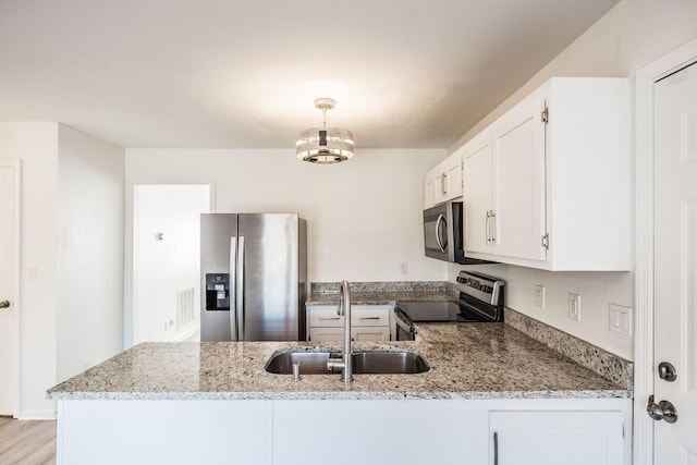 kitchen with a peninsula, appliances with stainless steel finishes, a sink, and white cabinets