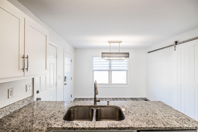 kitchen with light stone countertops, a barn door, pendant lighting, and a sink