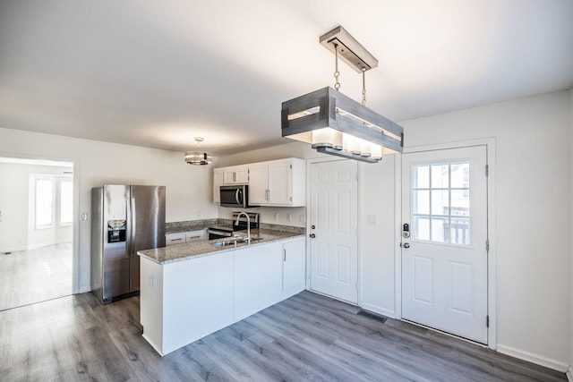 kitchen featuring a peninsula, stainless steel appliances, pendant lighting, and white cabinets