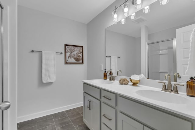 bathroom featuring double vanity, a shower stall, baseboards, and a sink