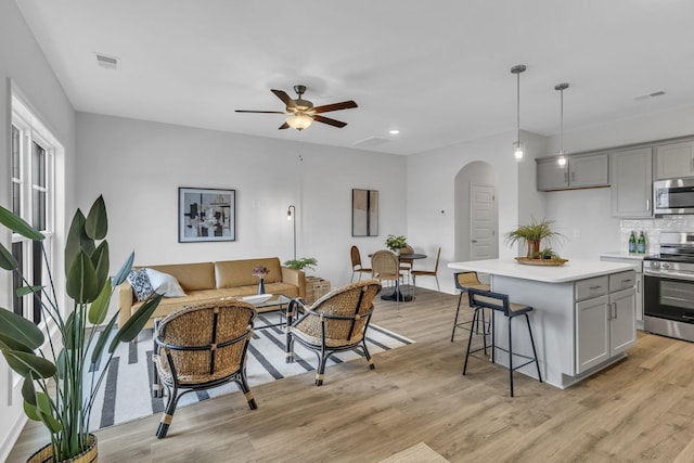 living area with light wood-style flooring, visible vents, arched walkways, and a ceiling fan