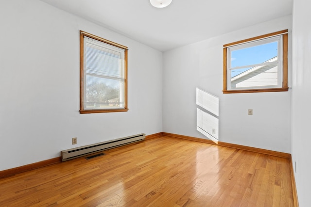 empty room with a baseboard heating unit, baseboards, visible vents, and light wood finished floors