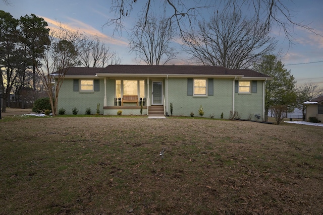 single story home with covered porch, brick siding, and a lawn