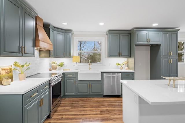 kitchen with stainless steel appliances, light countertops, custom range hood, and a sink