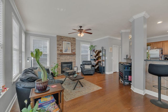 living room featuring crown molding, decorative columns, a large fireplace, wood finished floors, and baseboards