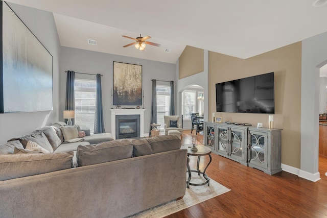living room with arched walkways, a glass covered fireplace, visible vents, vaulted ceiling, and dark wood finished floors