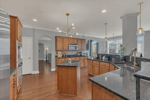 kitchen with arched walkways, stainless steel appliances, an island with sink, and decorative light fixtures