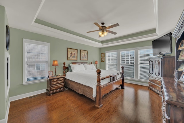 bedroom with visible vents, a tray ceiling, dark wood finished floors, and baseboards