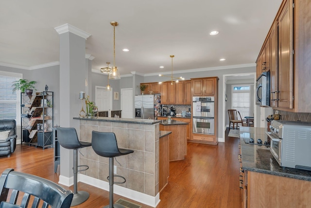 kitchen with stainless steel appliances, a breakfast bar, wood finished floors, brown cabinets, and decorative light fixtures