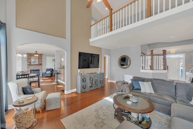 living area featuring baseboards, arched walkways, a ceiling fan, wood finished floors, and a stone fireplace