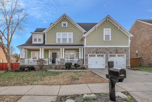 craftsman inspired home featuring covered porch, concrete driveway, fence, a garage, and stone siding