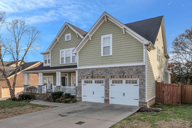 view of front of house featuring a porch, concrete driveway, fence, a garage, and stone siding