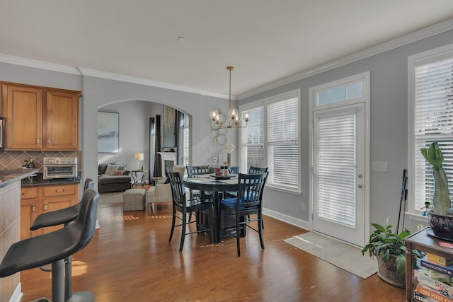 dining space featuring arched walkways, crown molding, baseboards, dark wood-style floors, and an inviting chandelier