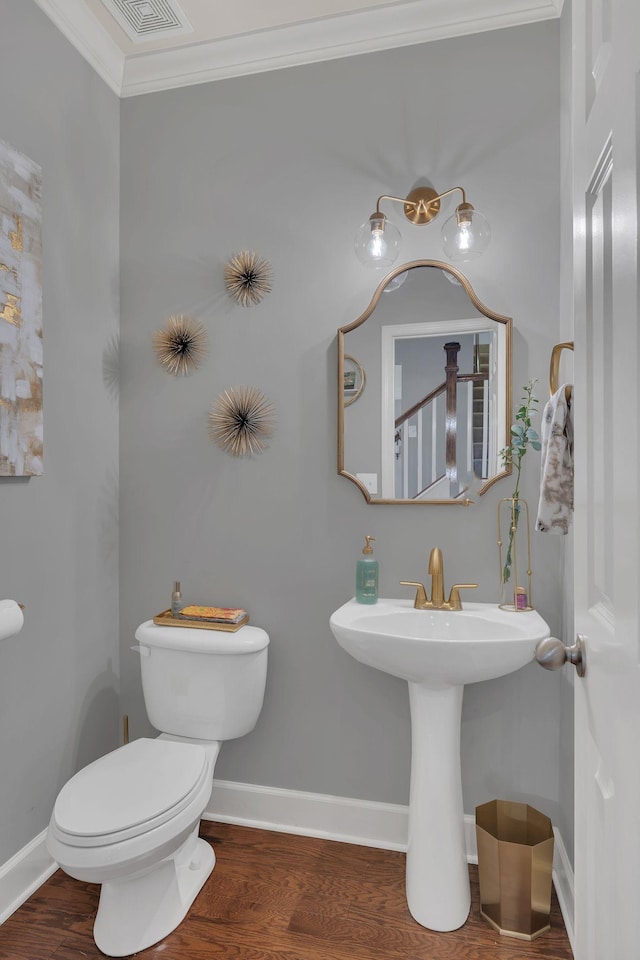 half bathroom featuring visible vents, baseboards, toilet, wood finished floors, and crown molding
