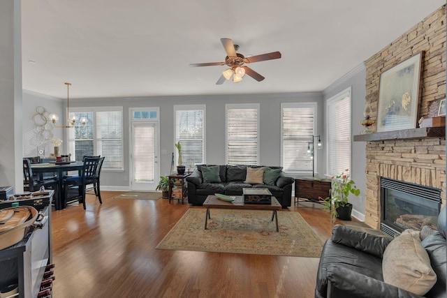 living area featuring ornamental molding, a stone fireplace, wood finished floors, and baseboards