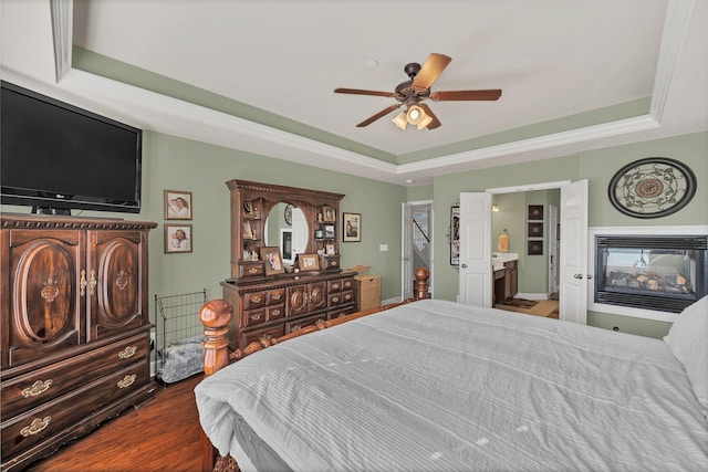 bedroom featuring a tray ceiling, dark wood finished floors, a multi sided fireplace, and ceiling fan