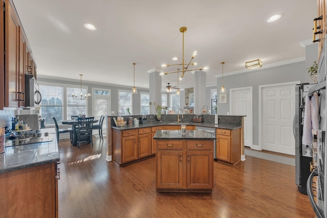kitchen with a peninsula, a center island, dark stone counters, brown cabinetry, and decorative light fixtures