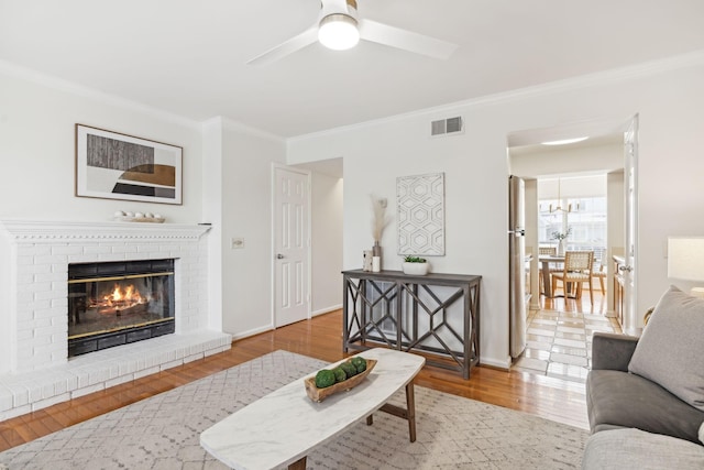 living room with a brick fireplace, visible vents, crown molding, and wood finished floors