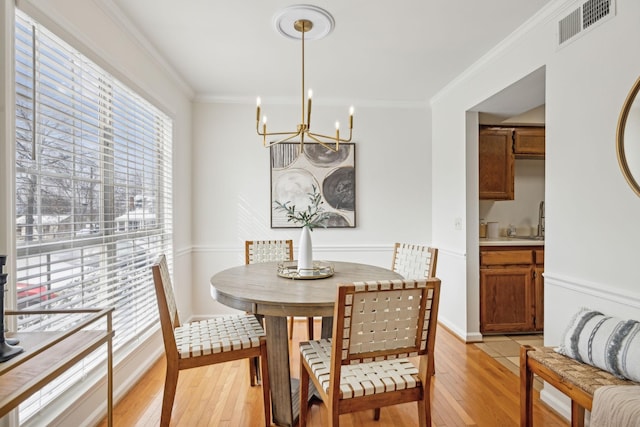 dining space with light wood finished floors, visible vents, a chandelier, and ornamental molding