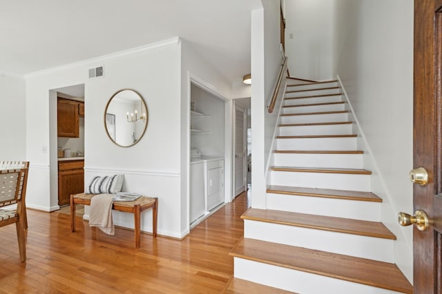 staircase with wood finished floors, visible vents, baseboards, washer and dryer, and ornamental molding