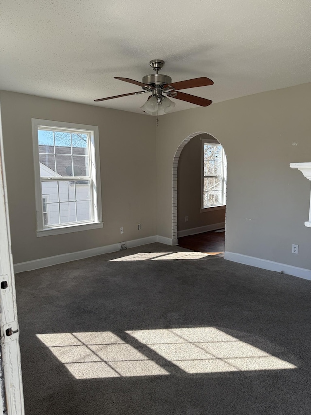 carpeted spare room featuring arched walkways, a textured ceiling, baseboards, and a ceiling fan