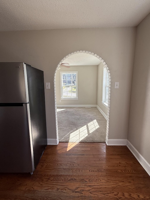 kitchen with arched walkways, a textured ceiling, wood finished floors, and freestanding refrigerator