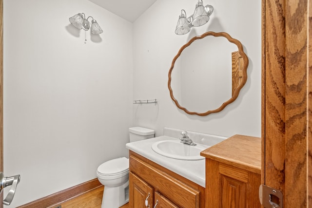 half bath with baseboards, toilet, wood finished floors, vanity, and a chandelier