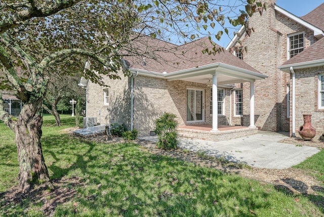 rear view of property featuring a patio area, a shingled roof, a lawn, and brick siding