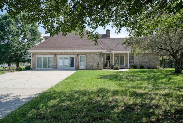view of front of house featuring brick siding, a chimney, a shingled roof, concrete driveway, and a front yard