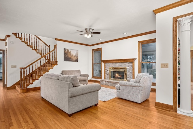 living room with a fireplace, light wood finished floors, stairway, ornamental molding, and ornate columns