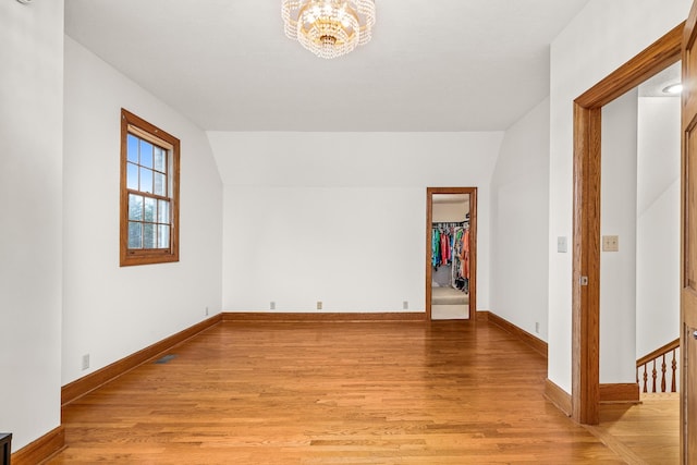 empty room featuring lofted ceiling, light wood finished floors, baseboards, and a chandelier