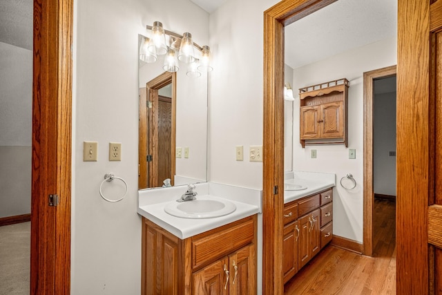 bathroom featuring wood finished floors, two vanities, a sink, and baseboards