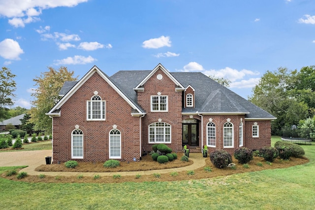 view of front facade with a shingled roof, a trampoline, a front lawn, and brick siding