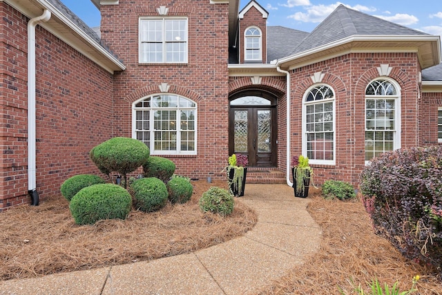 entrance to property featuring brick siding, roof with shingles, and french doors