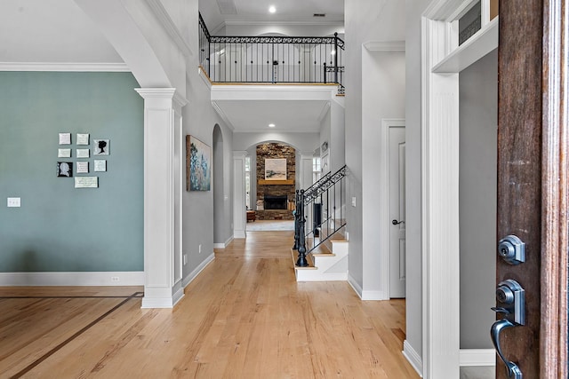 entryway featuring arched walkways, a stone fireplace, light wood-style floors, ornamental molding, and decorative columns