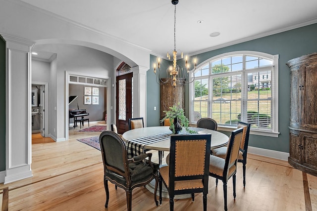 dining space featuring arched walkways, ornate columns, an inviting chandelier, light wood-type flooring, and baseboards