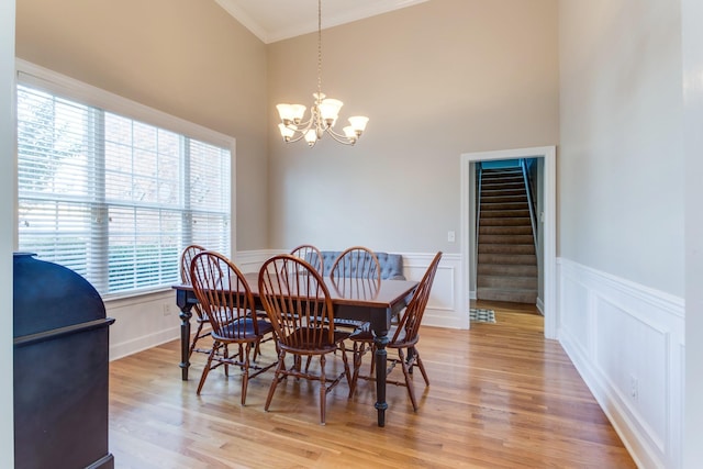 dining room featuring light wood-style flooring, stairway, ornamental molding, a chandelier, and a decorative wall