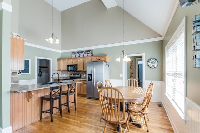 dining area featuring visible vents, wainscoting, an inviting chandelier, light wood-type flooring, and high vaulted ceiling