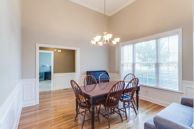 dining area with a chandelier, light wood-type flooring, a wainscoted wall, and crown molding