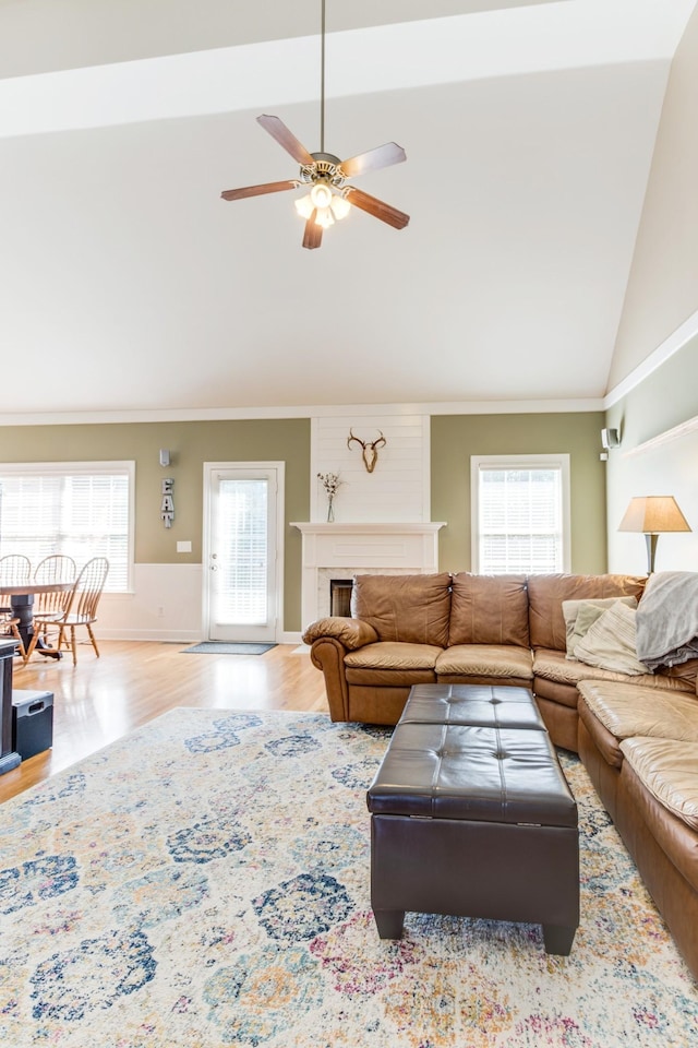 living area featuring a fireplace, a ceiling fan, ornamental molding, wood finished floors, and high vaulted ceiling