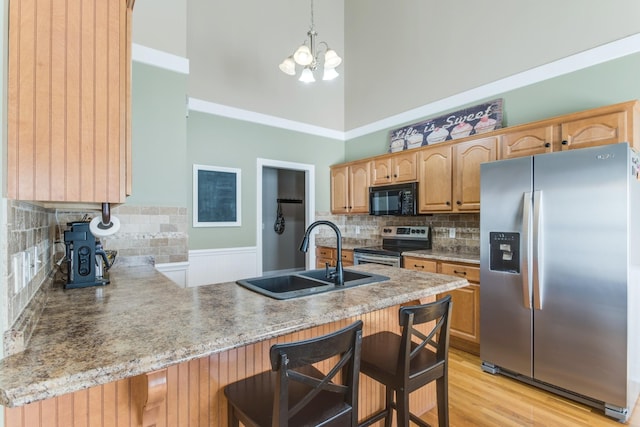 kitchen with light wood finished floors, a high ceiling, appliances with stainless steel finishes, a sink, and a peninsula