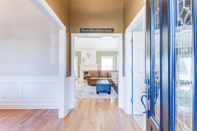 foyer with light wood-type flooring, wainscoting, a fireplace, and a decorative wall